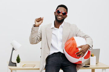 Joyful young man with dark skin, wearing red sunglasses and a beige blazer, holding a colorful...