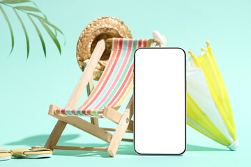 Mobile phone with mini chaise lounge, hat and umbrella on turquoise background