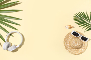Headphones with palm leaves, hat and sunglasses on beige background
