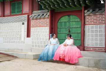 In June in Seoul, two Korean women in their twenties sit before a traditional wooden door of...