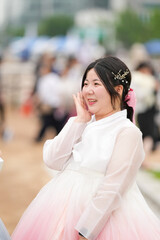 In Seoul in June 2025, a Korean woman in her twenties wearing a charming pink hanbok stands smiling...