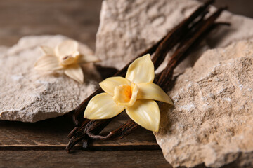 Dried vanilla sticks with flowers and stones on wooden background, closeup