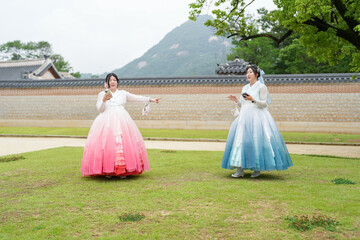 In Seoul in June 2025, two Korean women in their twenties wear pink and sky-blue hanbok as they...