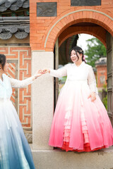 In Seoul in June 2025, two Korean women in their twenties wearing pink and sky-blue hanbok stand in...