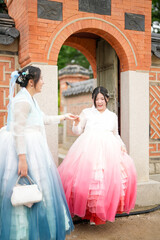 In Seoul in June 2025, two Korean women in their twenties wearing pink and sky-blue hanbok stand in...