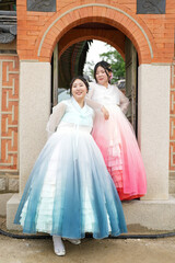 In Seoul in June 2025, two Korean women in their twenties wearing pink and sky-blue hanbok stand in...