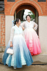 In Seoul in June 2025, two Korean women in their twenties wearing pink and sky-blue hanbok stand in...