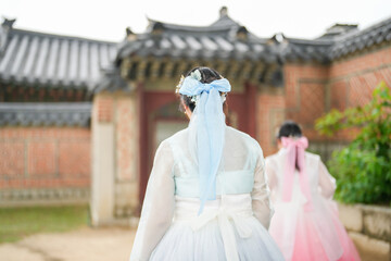 In Seoul in June 2025, two Korean women in their twenties wearing pink and sky-blue hanbok stand in...