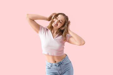 Cool young woman listening to music and dancing on pink background