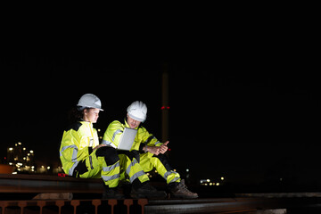 Engineers Collaborating on Site with Tablet in the Dark, Night Shift Crew Working on Industrial Project with Technology, Team of Workers Conducting Operations at Oil Storage Field Industrial Site