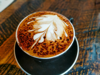 Mocha latte with leaf art pattern in dark cup on wooden table Ohio