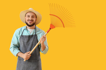 Male gardener with rake on yellow background