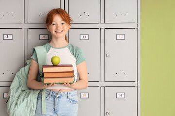 Teenage schoolgirl with apple and books near locker on green background