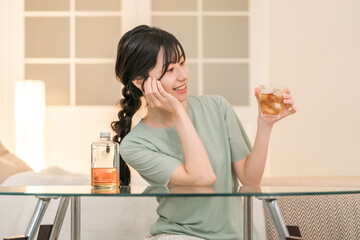 家の寝室で晩酌する若いアジア人女性（ウィスキー,家飲み,飲酒習慣）

