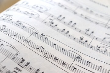 A white sheet with a musical partition. Musical notes on a sheet of music paper. Music notes as background with a close-up view.	