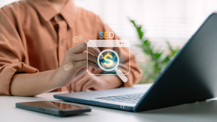 Fototapeta premium A businessman using a stylus and laptop with an SEO icon and dollar symbol on a virtual screen. Concept of search engine optimization, online marketing, and revenue growth strategy.