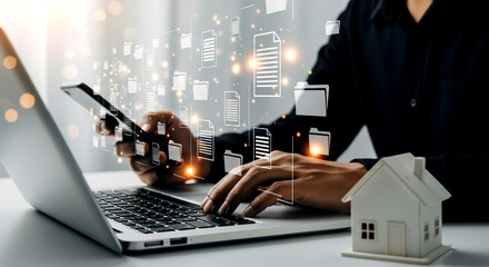 Person using laptop and phone with document icons and a miniature house on the table near them