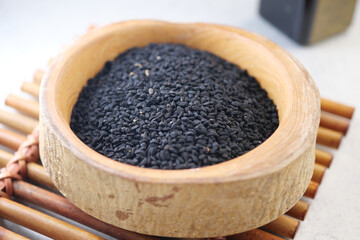 Black cumin seeds in a wooden bowl on a bamboo mat