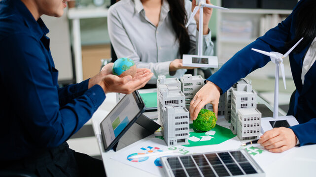 Business team presenting sustainable city model with solar panels, wind turbines, and Earth concept. Ideal for themes of green energy