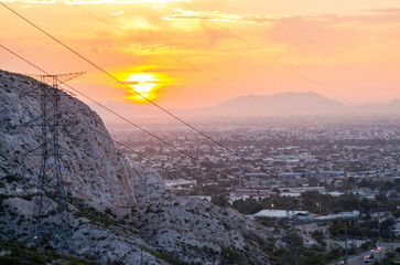 Stunning sunset paints the sky over city skyline, highlighting power lines and mountain landscape
