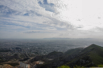 Breathtaking panoramic view of sprawling city nestled among rolling green mountains under cloudy sky