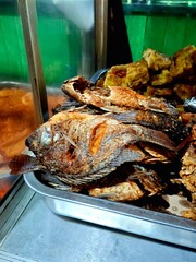 Fried mujahir fish, a traditional Javanese dish, sold in a simple display case at a traditional...