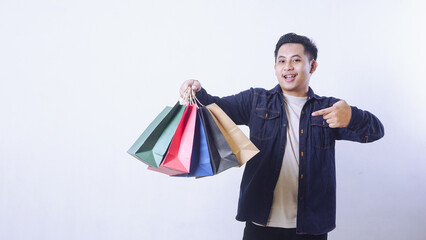 Portrait of Asian man holding shopping bags and pointing at it isolated on white background