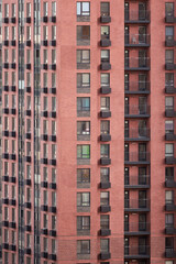 Fototapeta premium Facade Of A Modern Multi-Storey Residential Building With Red Brick Walls, Windows And Balconies. Urban Architecture Pattern And Texture. Vertical Shot.