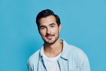 Smiling man with short dark hair wearing a light blue shirt against a solid turquoise background, looking directly at the camera with a friendly expression.