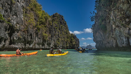 Tourist canoes sail through a beautiful turquoise lagoon surrounded by sheer cliffs. Tropical...