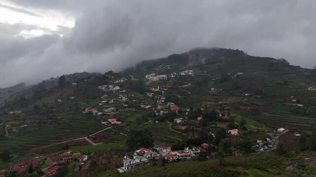Cinematic aerial pan of a hilly landscape with scattered farm plots and homes