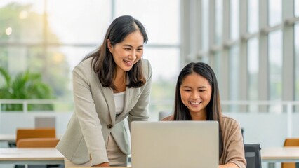 Two women engaged in a collaborative work session, smiling and discussing ideas in a modern office environment.