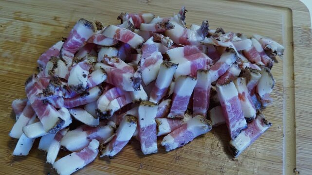 Top down orbit over diced guanciale cubes resting on wooden board, glistening with fat