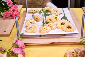 Soft peach lisianthus flowers arranged for pressing on a wooden flower press. Aesthetic flatlay on a vibrant yellow workspace — ideal for botanical DIY or floral crafts