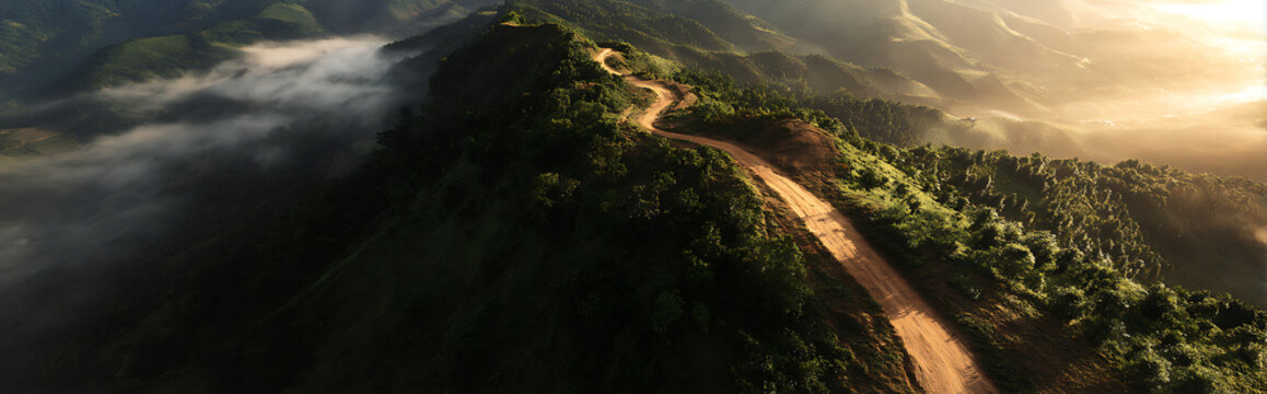 Aerial view of rugged muddy mountain trail with deep tracks under golden sunrise light, morning mist and fog creating dramatic topographic map effect in wilderness landscape. - Powered by Adobe