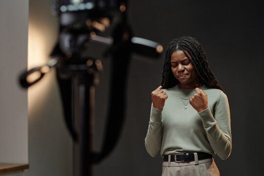 Young adult Black woman standing in front of camera clenching fists and expressing intense emotion during acting audition, performing dramatic scene with closed eyes