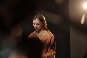 Caucasian young adult man standing in studio setting preparing for acting audition looking down with focused expression soft lighting highlighting facial features