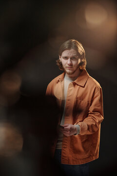 Caucasian young adult man standing on stage holding script, performing monologue during acting audition, looking slightly past camera with focused facial expression, dramatic lighting