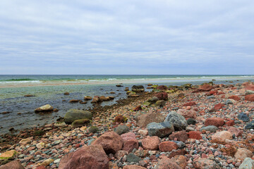 Path of Silence.
A rocky shoreline stretches alongside a calm, slightly greenish sea. Every boulder and pebble seems to tell a story carved by time and tide. 
