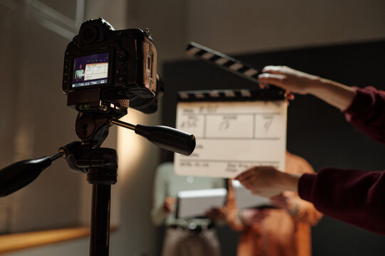 Two young adult individuals standing in front of camera holding scripts while crew member holding clapperboard, preparing for acting audition in studio setting