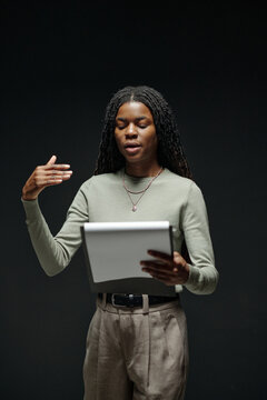 Black young adult woman standing and performing monologue while holding script during acting audition, gesturing with one hand and focusing on reading lines in studio setting
