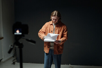 Young adult Caucasian man standing in front of camera holding script and preparing for acting audition, focused expression, studio setting, engaging with audition material