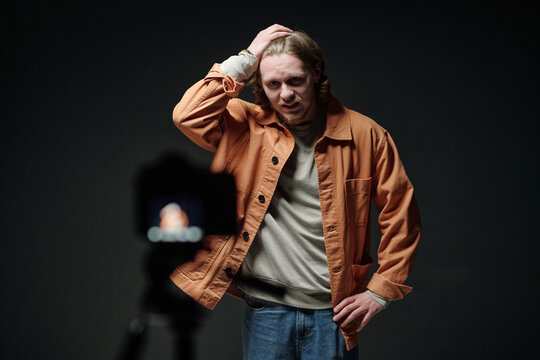 Caucasian young adult man standing in front of camera scratching head during acting audition, showing uncertain facial expression while performing scene for casting