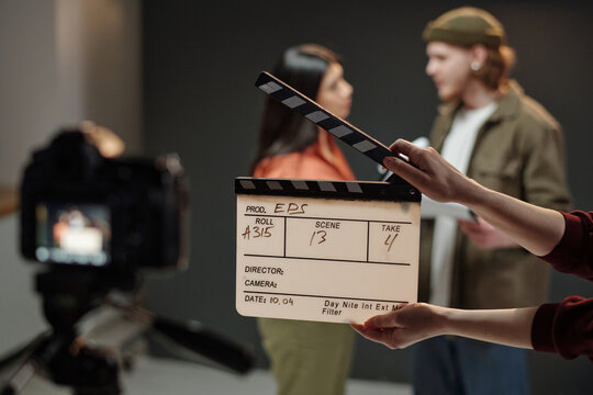 Hispanic woman and Caucasian young adult man rehearsing script during acting audition while crew member holding clapperboard in front of professional video camera