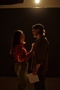 Hispanic woman and Caucasian man standing face to face rehearsing dramatic scene during acting audition, both holding scripts and engaging in intense eye contact