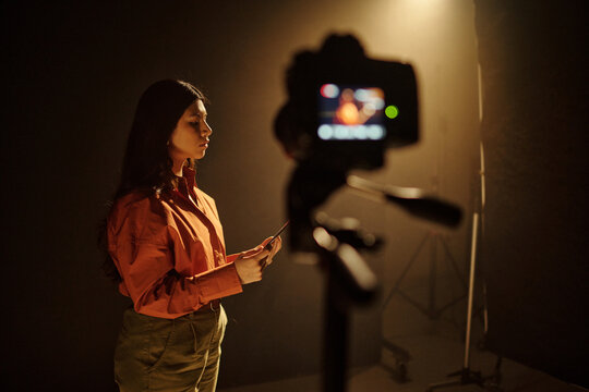 Young adult Hispanic woman standing in front of camera holding script performing audition on professional set, focused expression, studio lighting highlighting subject during acting audition