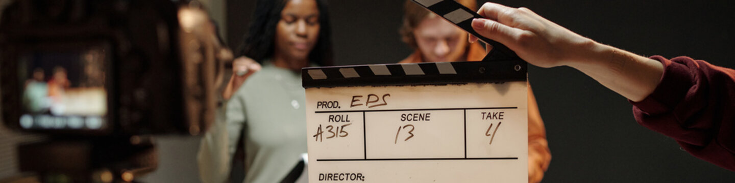 Multiethnic young adults preparing for acting audition, standing behind film slate while crew member holding clapperboard, camera recording scene in professional studio setting