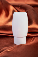 Cosmetic product in tube, bottle, lotion or serum on shiny cloth background