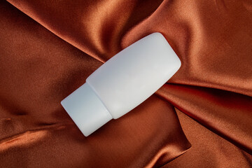 Cosmetic product in tube, bottle, lotion or serum on shiny cloth background