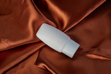 Cosmetic product in tube, bottle, lotion or serum on shiny cloth background
